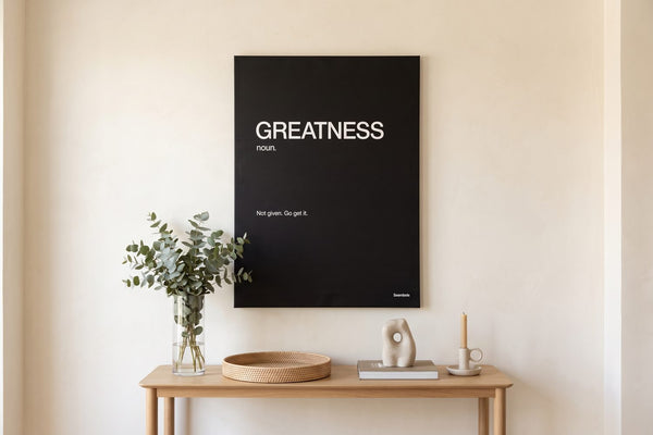 Acrylic vs canvas print: a Greatness Definition canvas above an oak console with eucalyptus and a rattan tray