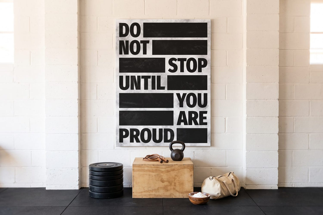 Gym quotes: a Do Not Stop Until You Are Proud canvas in a white brick garage gym with weight plates and a kettlebell