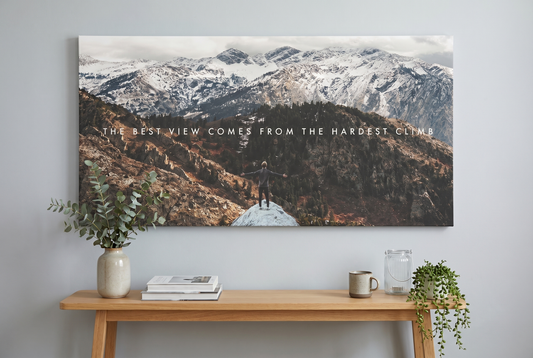 Mountain wall art: The Climb canvas above an oak console with eucalyptus and stacked books