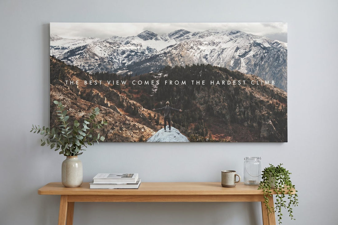Mountain wall art: The Climb canvas above an oak console with eucalyptus and stacked books