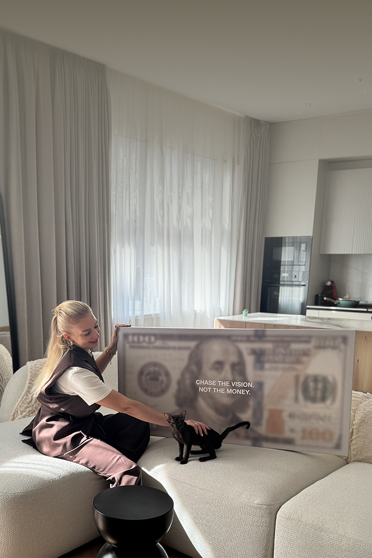 Person sitting on a couch with a large dollar bill canvas art and a cat in a modern living room.