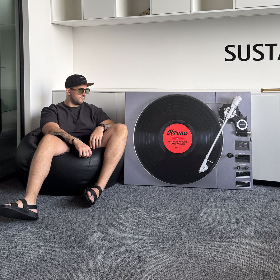 Man sitting on a bean bag next to a record player Seembols canvas art with a vinyl record printed on it in a modern office room.