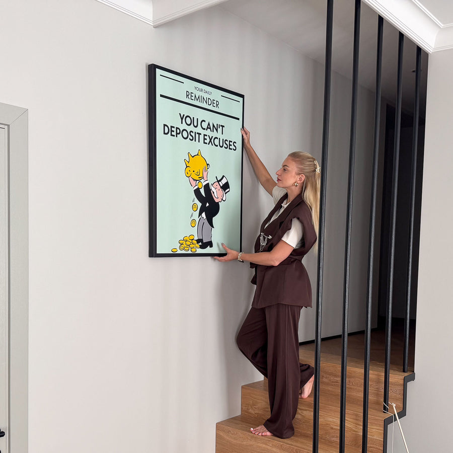 Woman hanging a motivational Monopoly canvas art You Can't Deposit Excuses on a wall.
