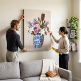 Couple hanging the Baseball Vase canvas in a living room, one pointing with a spirit level