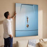 Man in a white linen shirt adjusting the Car Dive canvas on a sand colored wall above a cream sofa