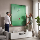 Two men hanging the Car Putt canvas above a white media cabinet in a taupe living room