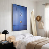Car Surfing canvas above a bed in a white paneled beach house bedroom with a longboard and a straw hat