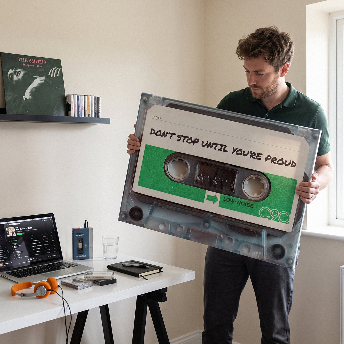 Man in a green knit polo holding the Don't Stop Until You Are Proud cassette canvas in his home office