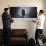 Two men hanging the Endure The Arena lion quote canvas above a leather sofa