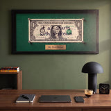 First Dollar money wall art above a walnut desk in a green home office