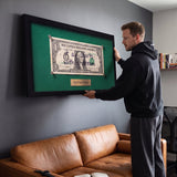 Man hanging the First Dollar canvas above a tan leather sofa