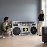 Couple checking the wide Make Happiness Louder boombox canvas leaning on the floor of a grey living room