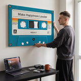 Young man hanging the Make Happiness Louder cassette canvas above his desk in an off-white home office