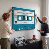 Two men leveling the Make Happiness Louder cassette canvas on a pale grey wall above a boombox