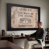 Man working at a laptop below the Man In The Arena ticket canvas in a home office
