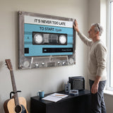 Person working at a desk below the Never Too Late blue cassette canvas
