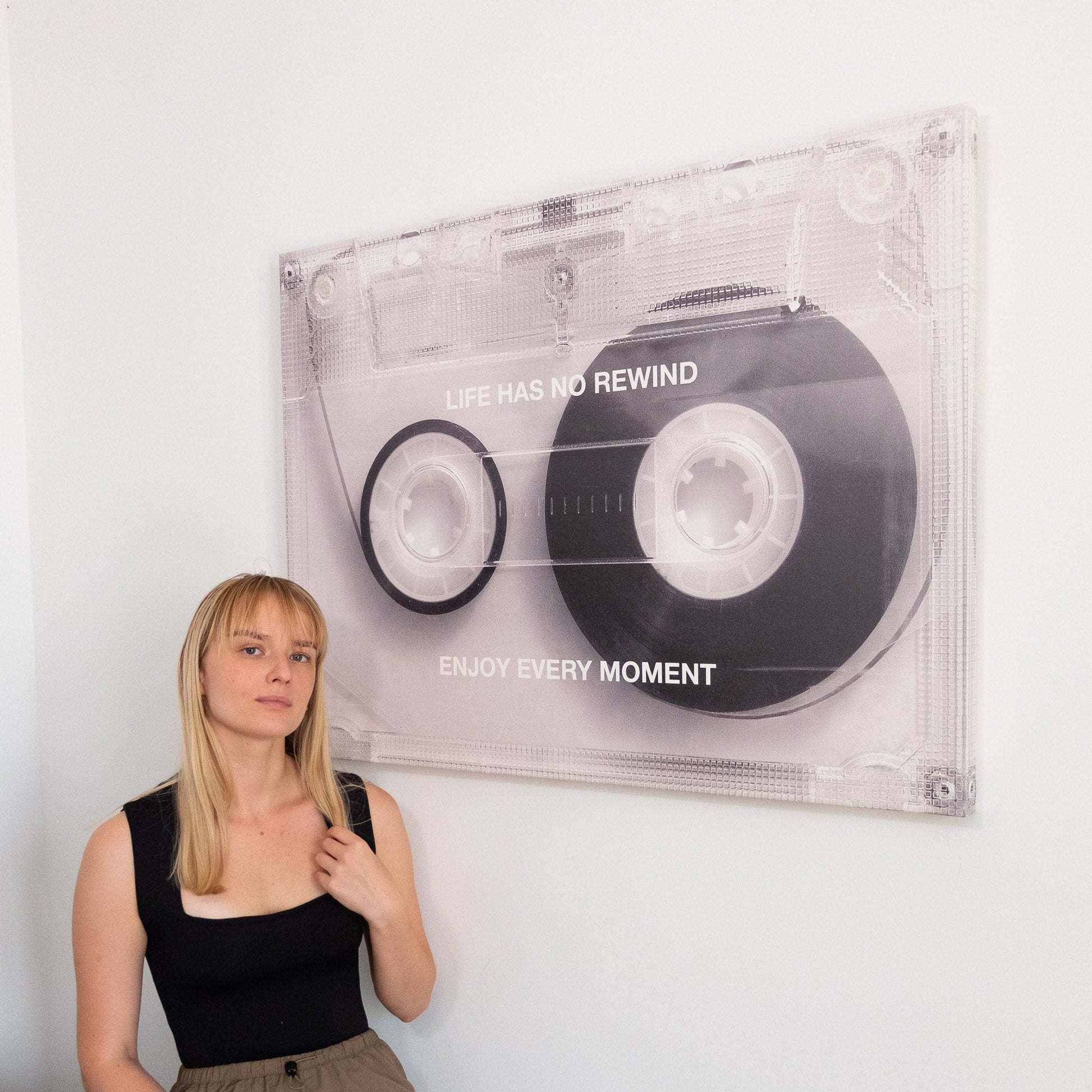 Person standing next to a large Life Has No Rewind cassette canvas art with text on a white wall
